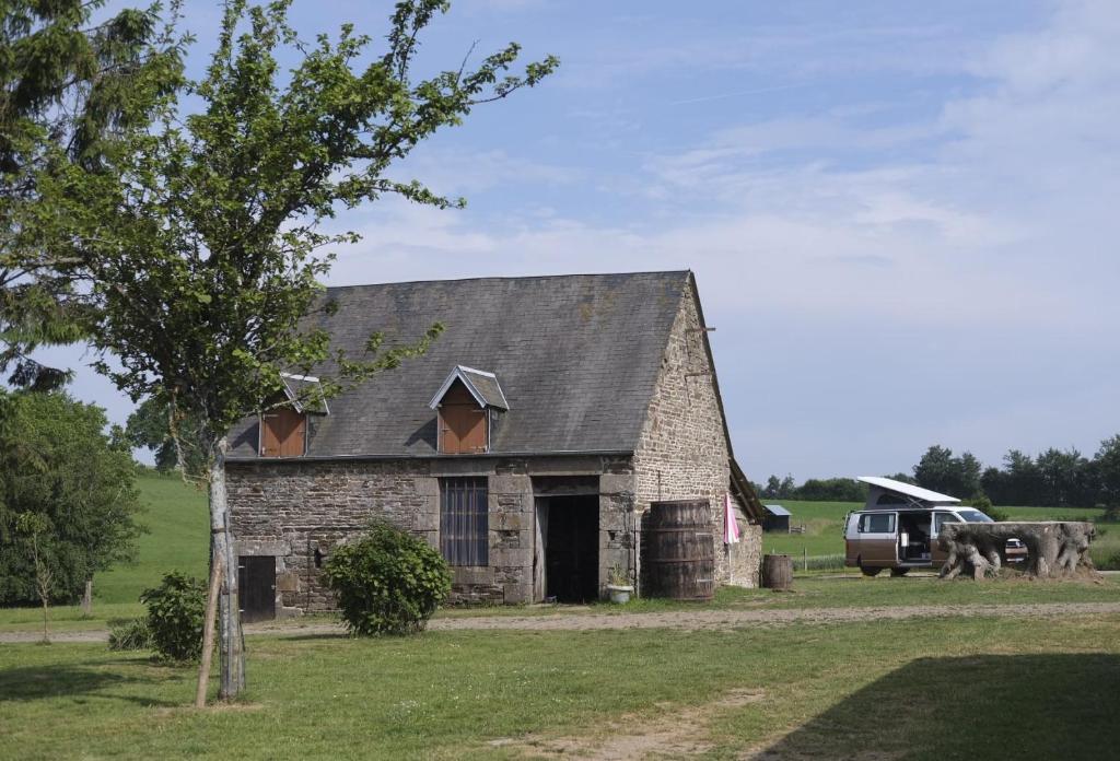 une ancienne grange en pierre avec un camion garé dans un champ dans l'établissement La Billardière Camping à la Ferme, à Le Ménil-Ciboult