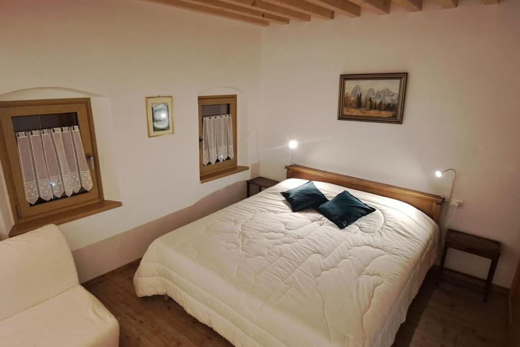 a bedroom with a white bed with two blue pillows at Nonna Clara, monolocale in Pieve di Cadore