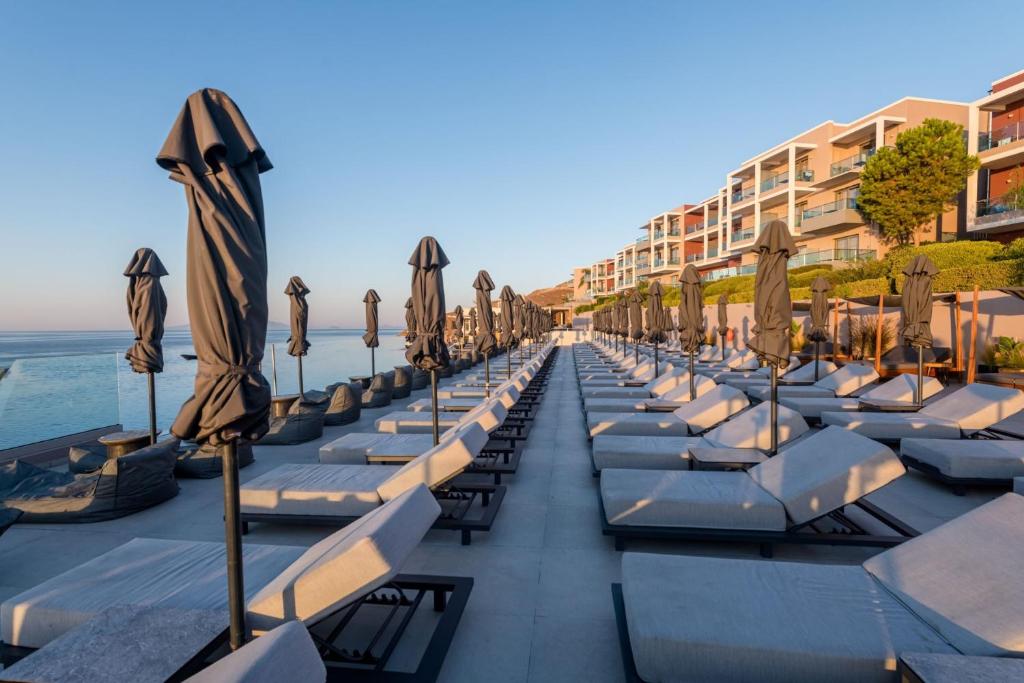 a row of lounge chairs with umbrellas on a beach at Michelangelo Resort & Spa in Ágios Fokás