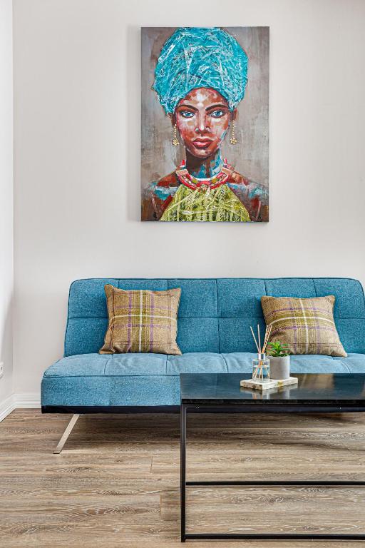a blue couch in a living room with a painting of a woman at ARI Olive Apartment near Atrium & AFI Mall in Arad