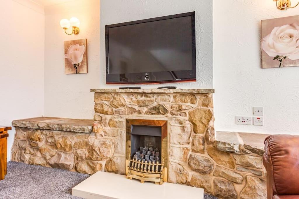 a living room with a stone fireplace with a flat screen tv at Delightful Garforth Home in Garforth