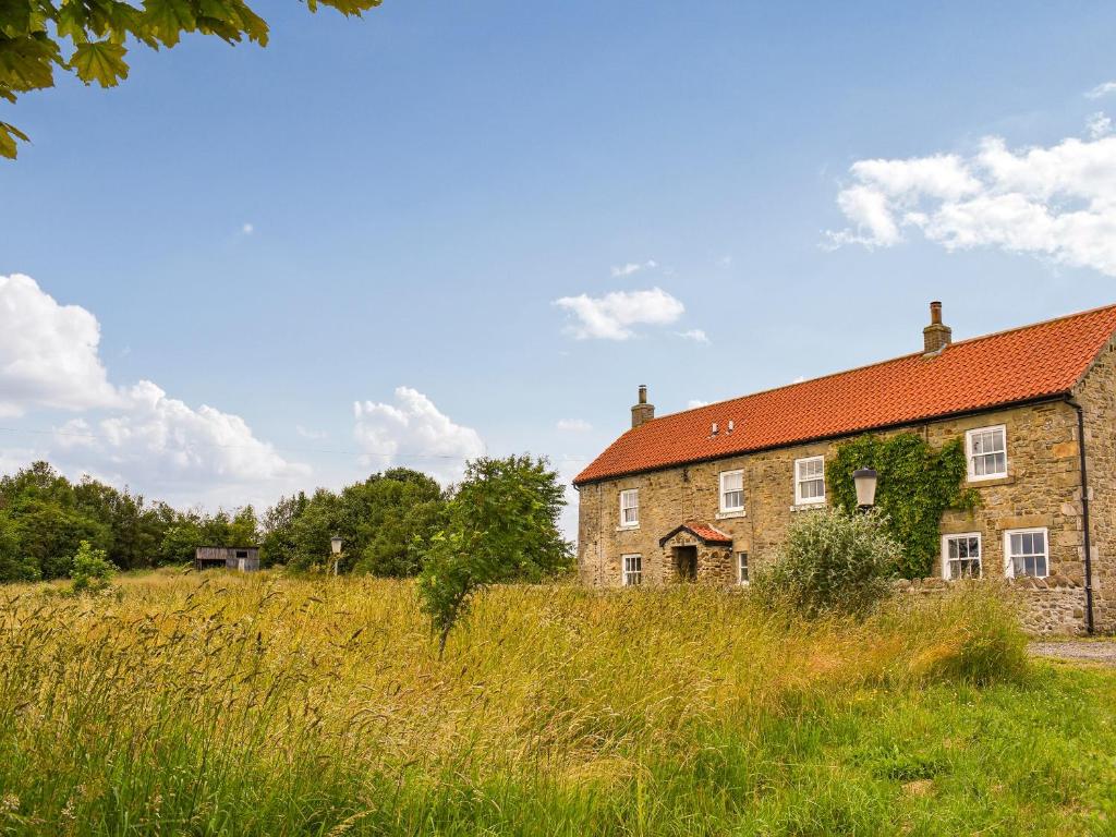 an old brick building with a red roof in a field at High Bank Farm in Cockfield