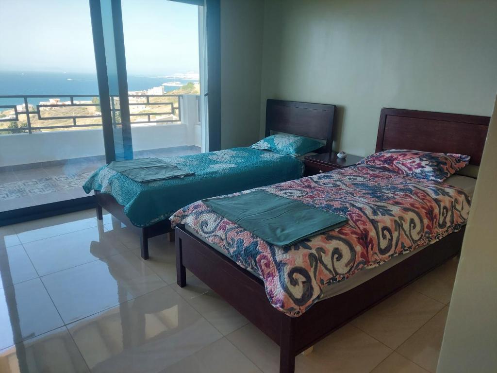 two beds in a room with a view of the ocean at Ghougine Serenity Residence Bis in Tangier