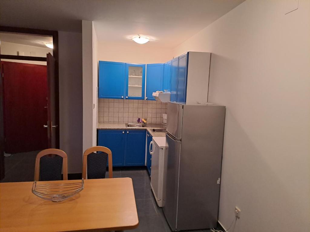 kuchnia z niebieskimi szafkami, stołem i lodówką w obiekcie Apartman zarok w Bašce
