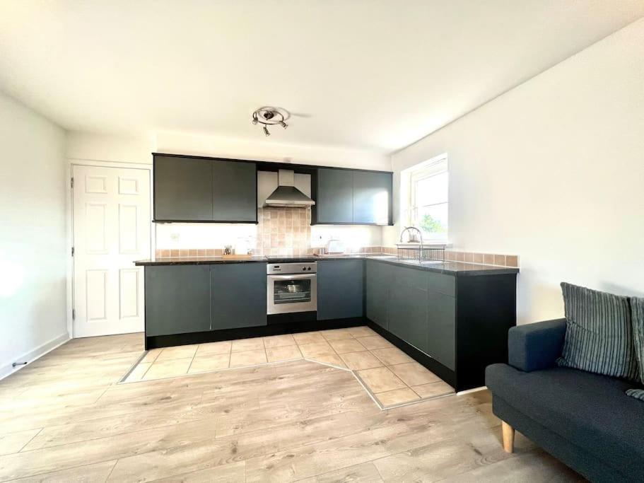 a kitchen with black cabinets and a blue couch at Cosy apartment in town centre in Finedon