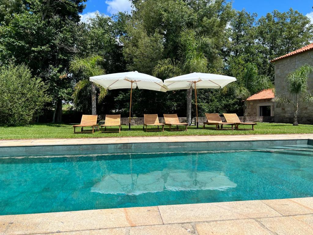 ein Pool mit zwei Sonnenschirmen und zwei Stühlen in der Unterkunft Quinta do Moinho da Ínsua in Ponte de Lima