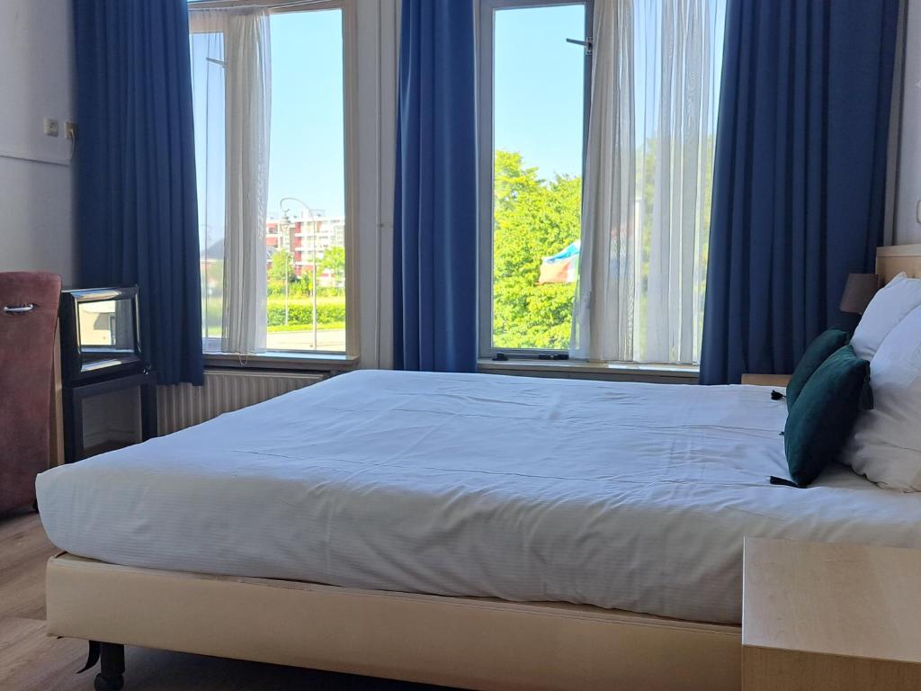 a bedroom with a large bed with blue curtains and windows at Hotel Restaurant Boven Groningen in Delfzijl