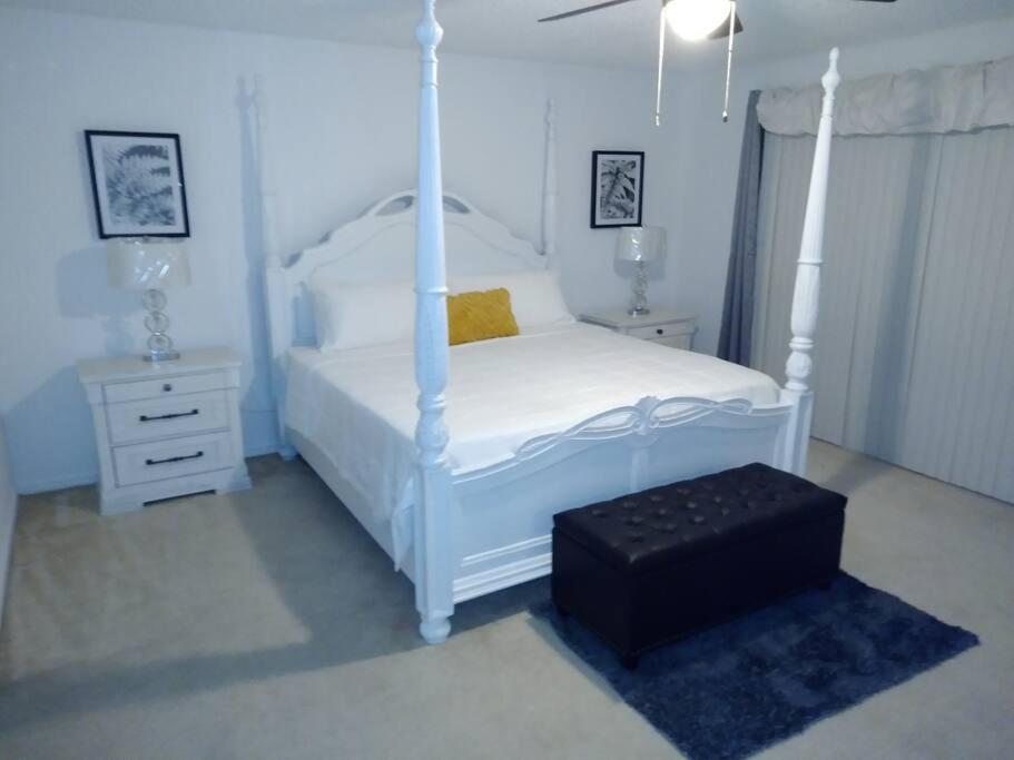 a white bedroom with a canopy bed and a stool at Amore's luxurious 4 bedroom home. in Kissimmee