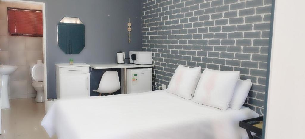 a bedroom with a white bed and a brick wall at Mels in Richards Bay