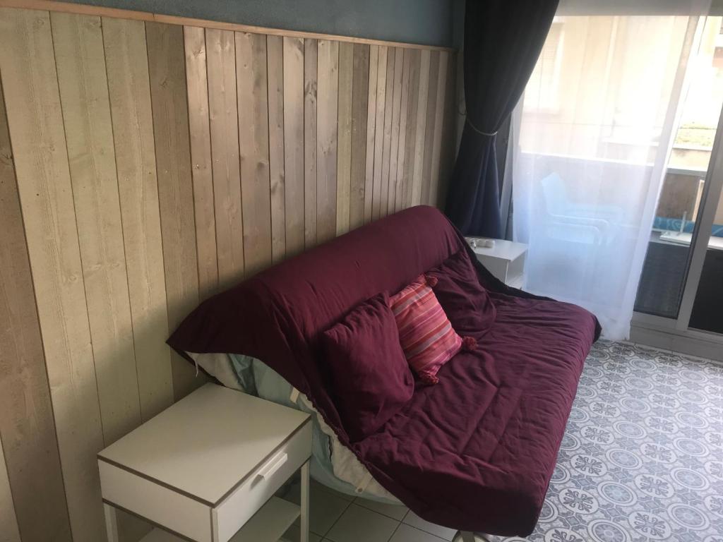 a small bed with a red blanket and a table at Location Sète les pieds dans l&#39;eau in Sète