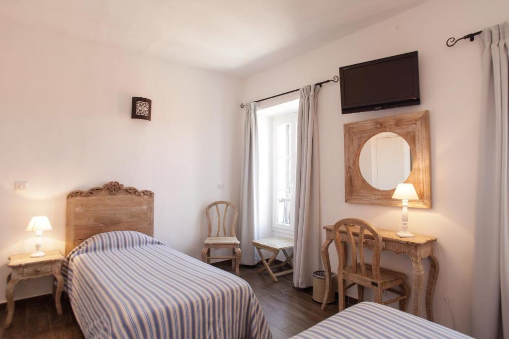 a bedroom with two beds and a mirror and a window at Hôtel de la Plage Les Arcades in Algajola