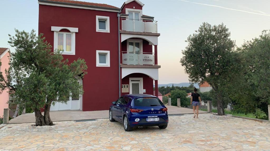 a blue car parked in front of a red building at Villa Hercegovina in Sveti Filip i Jakov