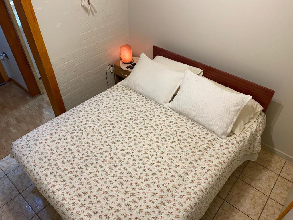 Una cama con almohadas blancas y una lámpara en una mesa. en Alojamiento Sandra - Habitación 02 en Villarrica