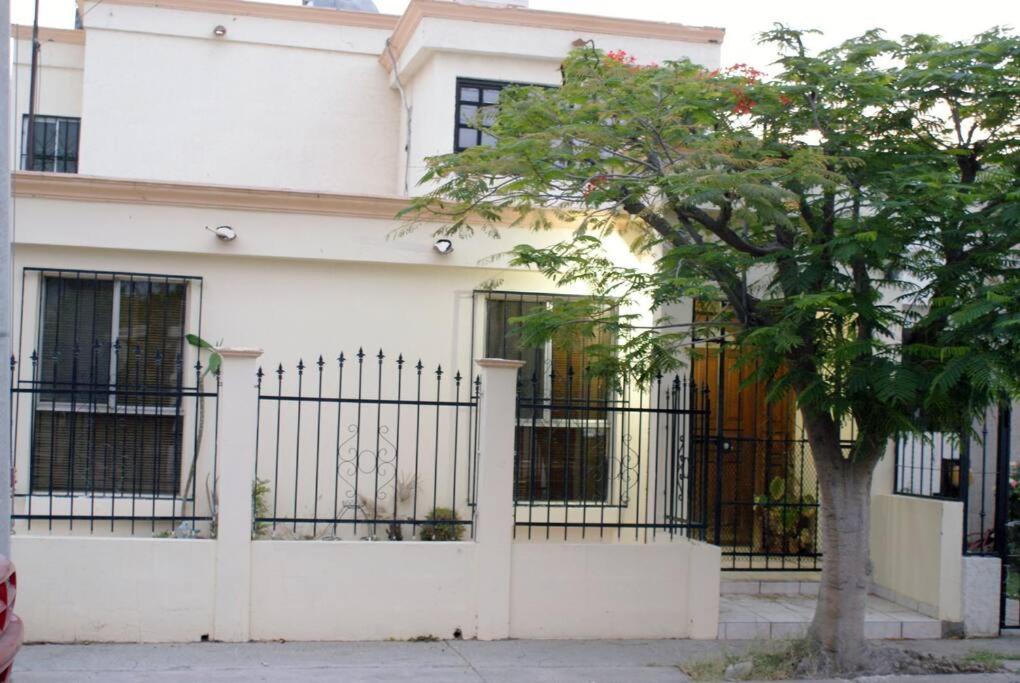 ein weißes Haus mit einem Tor und einem Baum in der Unterkunft Encantadora casa con 3 habitaciones frente al parque in Hermosillo