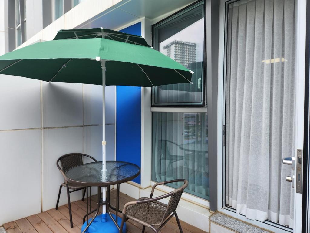a table and chairs with a green umbrella on a balcony at Well stay in Incheon