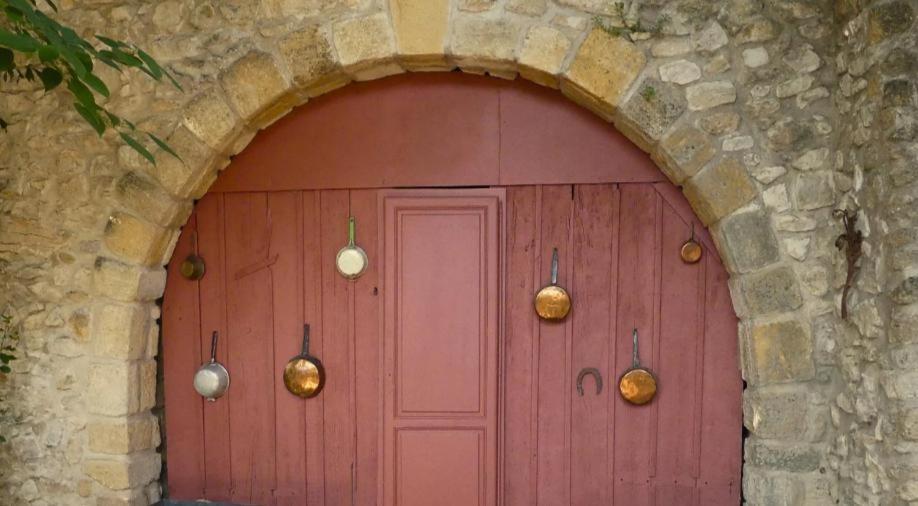 Una puerta roja en un edificio de piedra con campanas. en Chambre d'hôtes, en Lançon-Provence