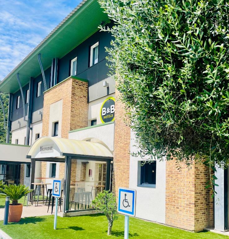 un bâtiment avec un panneau pour personnes à mobilité réduite devant lui dans l'établissement B&B HOTEL Aubagne Gémenos, à Gémenos
