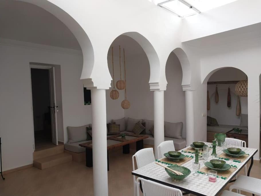 ein Esszimmer und ein Wohnzimmer mit einem Tisch und Stühlen in der Unterkunft Riad plain pied 2 chambres jardin terrasse & bassin in Tamraght Ouzdar