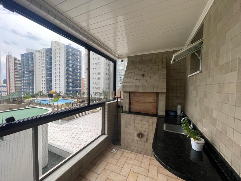 einen Balkon mit einem Waschbecken und einem großen Fenster in der Unterkunft Apto a 30m da praia sobre shopping Atlântico in Balneário Camboriú