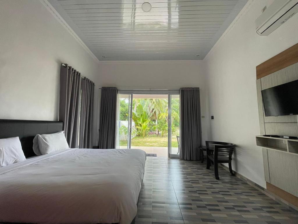 a bedroom with a bed and a tv and a sliding glass door at PONDOK SAHANG COTTAGES in Muntok