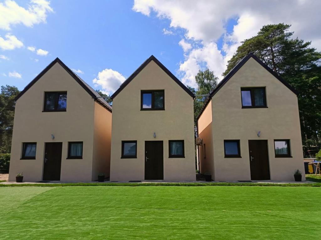 two white houses with black doors on a green field at Lawendowe Domki i Apartamenty w Pobierowie in Pobierowo