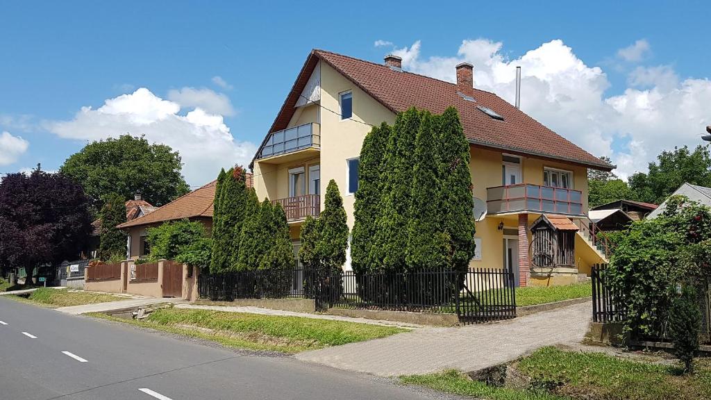 una casa amarilla con una valla negra y árboles en Großes Ferienhaus Plattensee Balaton - nyaraló ház 6 szobával, 5 fürdőszobával, 3000 nm, en Szólád
