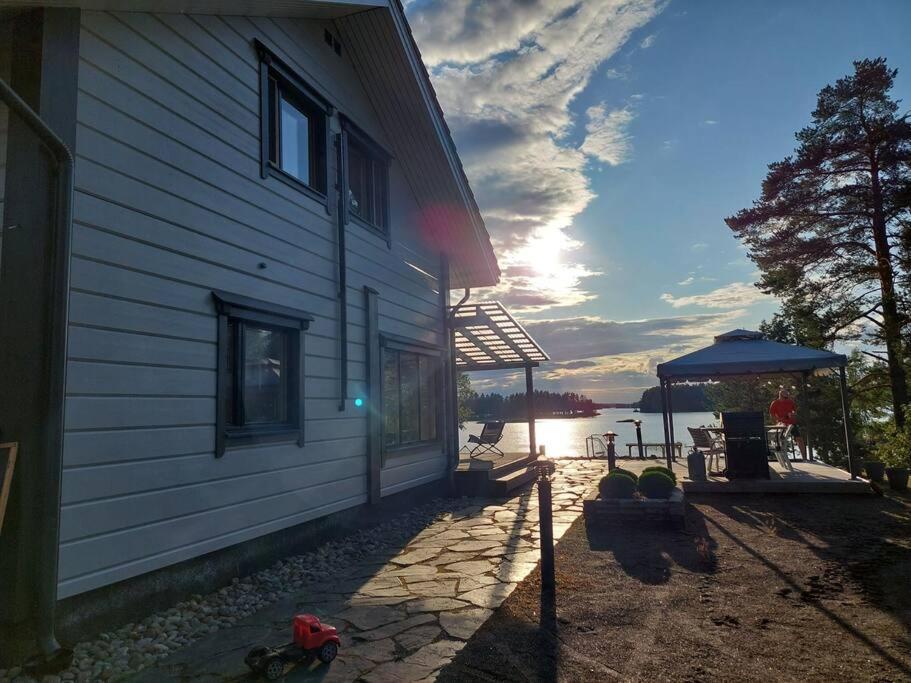 a house with the sun setting next to the water at Villa Mustalahti in Mikkeli