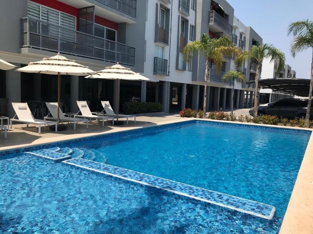Una piscina con sillas y sombrillas al lado de un edificio. en BONITO DEPA ! Cerritos a 2 Cuadras de PLAYA, en La Florida