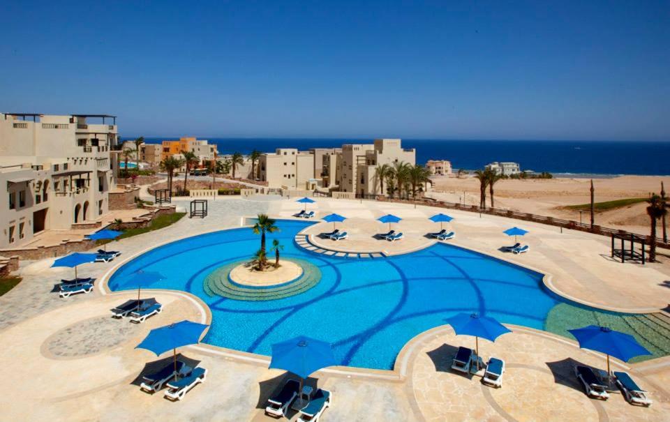 a large pool with blue umbrellas and chairs and the beach at Azzurra Sahl Hasheesh in Hurghada