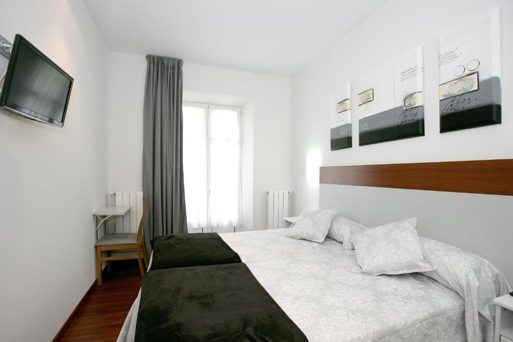 a white bedroom with a bed and a television at Hostal San Ignacio Centro in San Sebastián