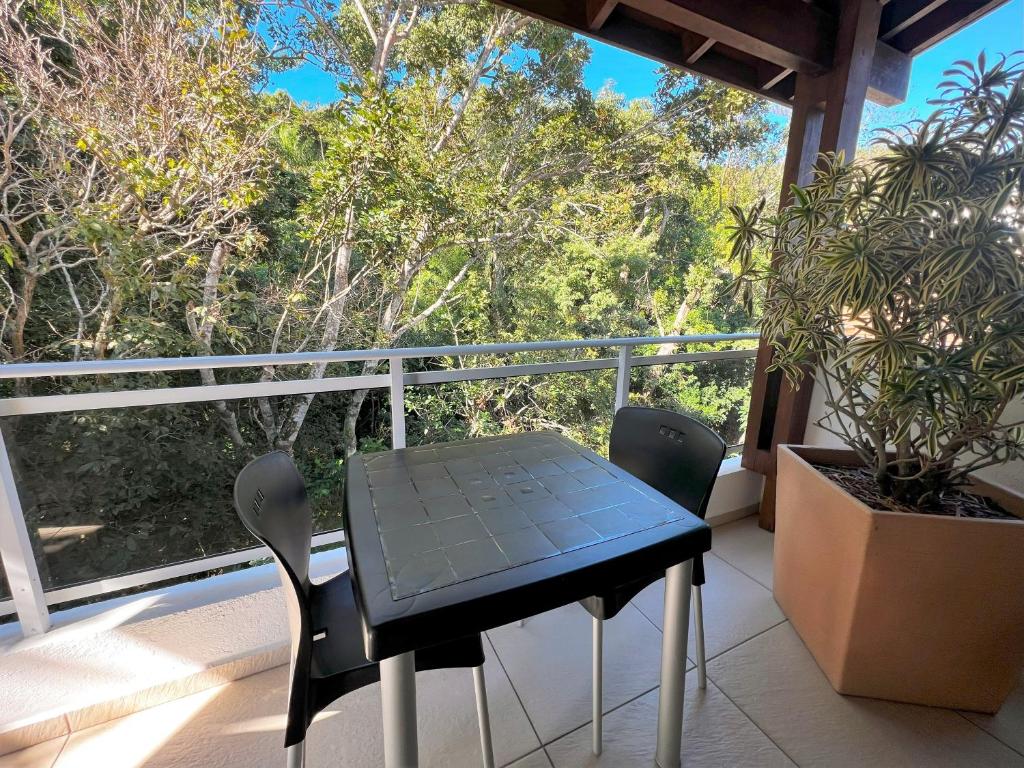 a table and chairs on a balcony with a view of trees at Refúgio da Lagoinha - Centro de Bombinhas in Bombinhas