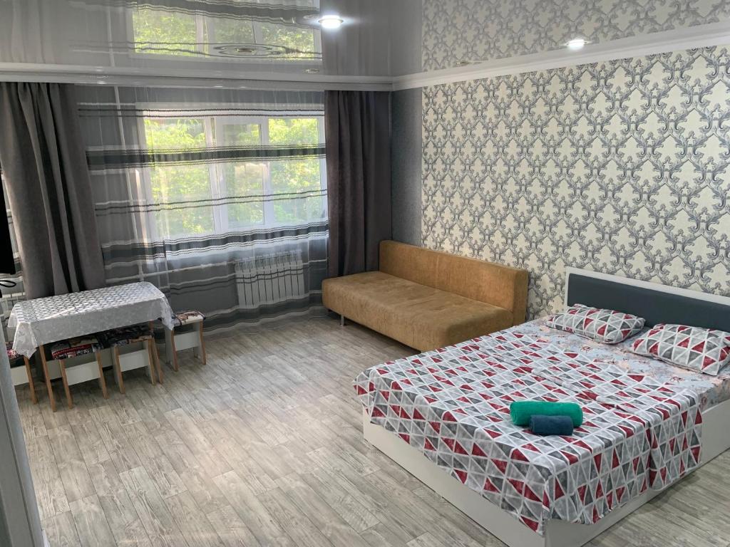 a bedroom with a bed and a couch and a window at IZUMRUD in Petropavlovsk