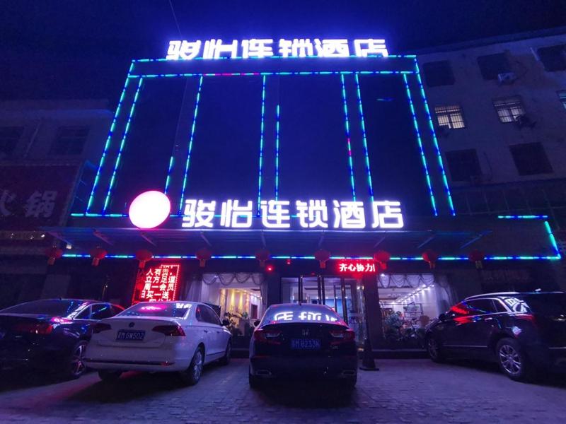 JUN Hotels Shanxi Yuncheng Yongji Bus Station في يونتشنغ: مبنى مضاء فيه سيارات متوقفة أمامه