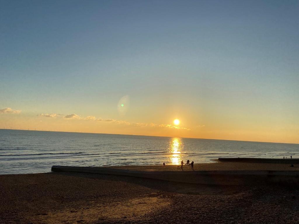 a sunset over the ocean with people walking on the beach at The Windsor Apartment by GGE, Brighton Beach, Sleeps 4 in Brighton & Hove