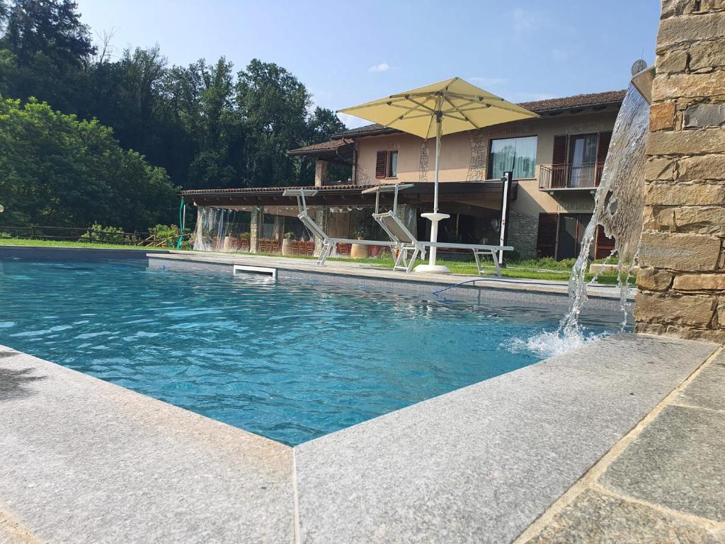 a swimming pool with a fountain in front of a house at Agriturismo Cascina L'Arché in Santo Stefano Belbo