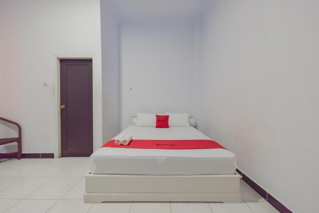 Bett in einem weißen Zimmer mit einer roten Decke in der Unterkunft RedDoorz Syariah near Ramayana Mall Tarakan in Tarakan