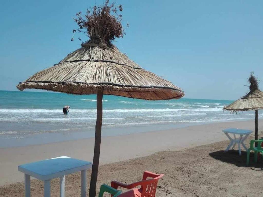 a beach with chairs and an umbrella and the ocean at Résidence Nydia in Ras El Ma