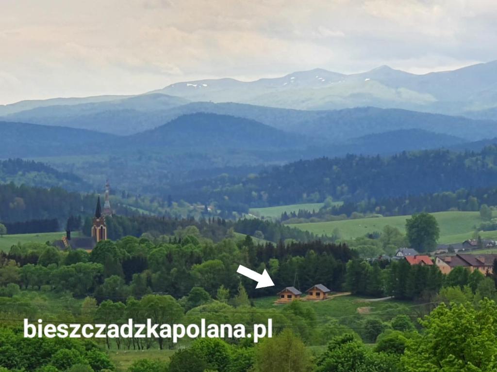a view of a valley with a church and mountains at Bieszczadzka Polana - domki turystyczne/sezonowe in Lutowiska