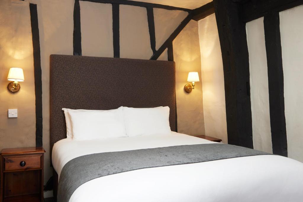 um quarto com uma cama grande e lençóis brancos em Bull Hotel by Greene King Inns em Halstead