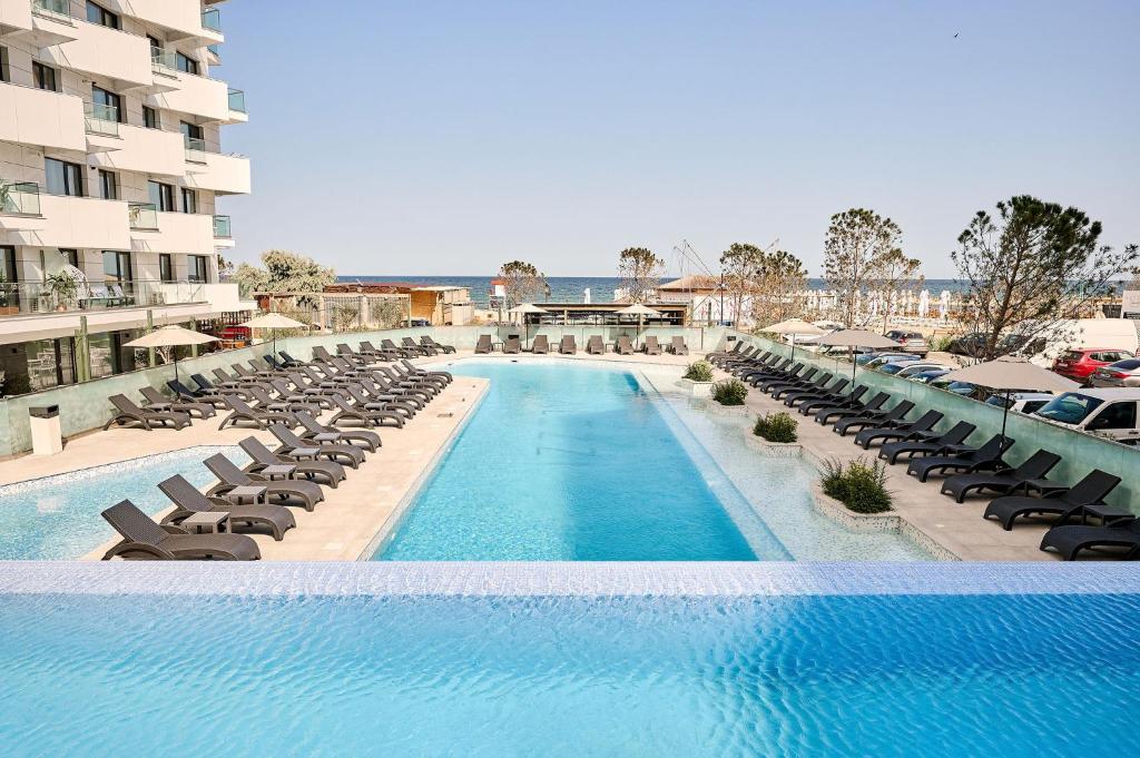 una piscina con tumbonas y sillas en Infinity Everglow Apartment Spa&Pool Beach Resort-parking, en Mamaia