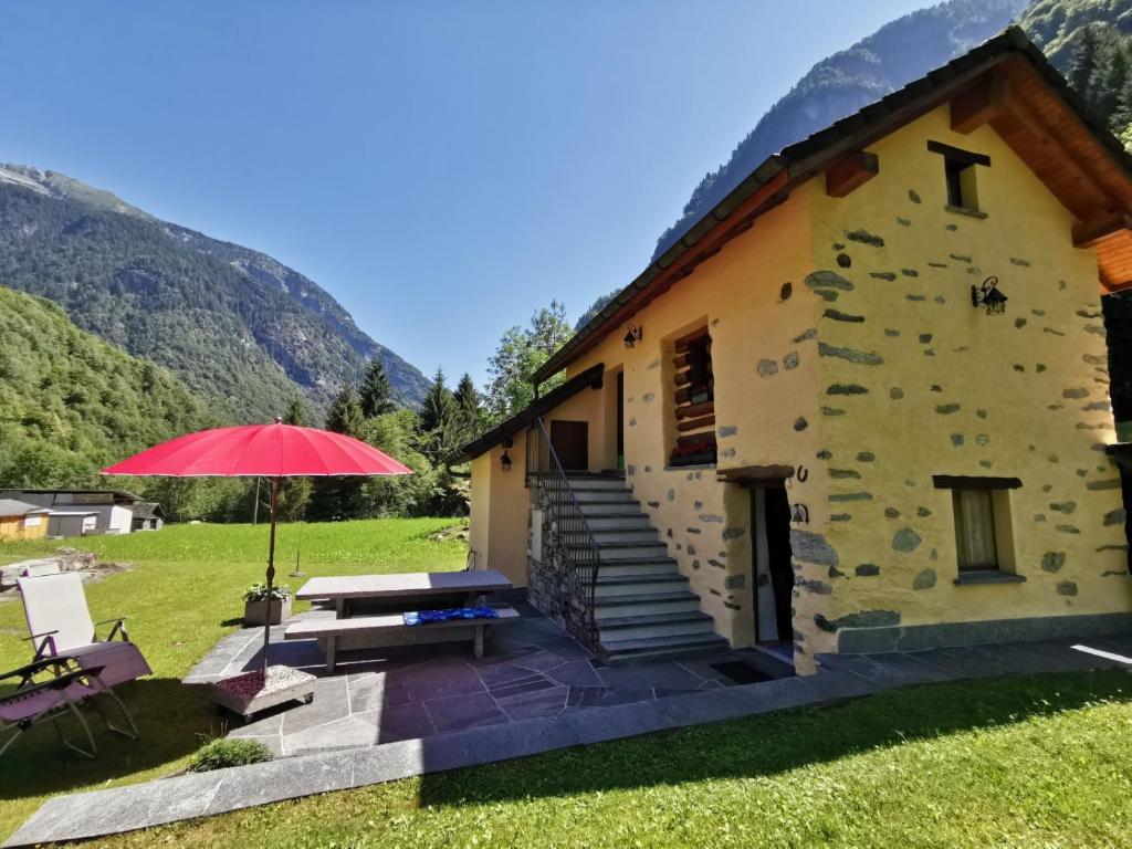 un edificio con sombrilla roja, mesa y banco en Ca da Lovi, en Cerentino