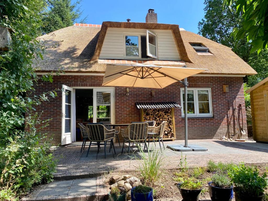 un patio con mesa, sillas y sombrilla en Huisje aan de Bosrand - Veluwe, en Epe