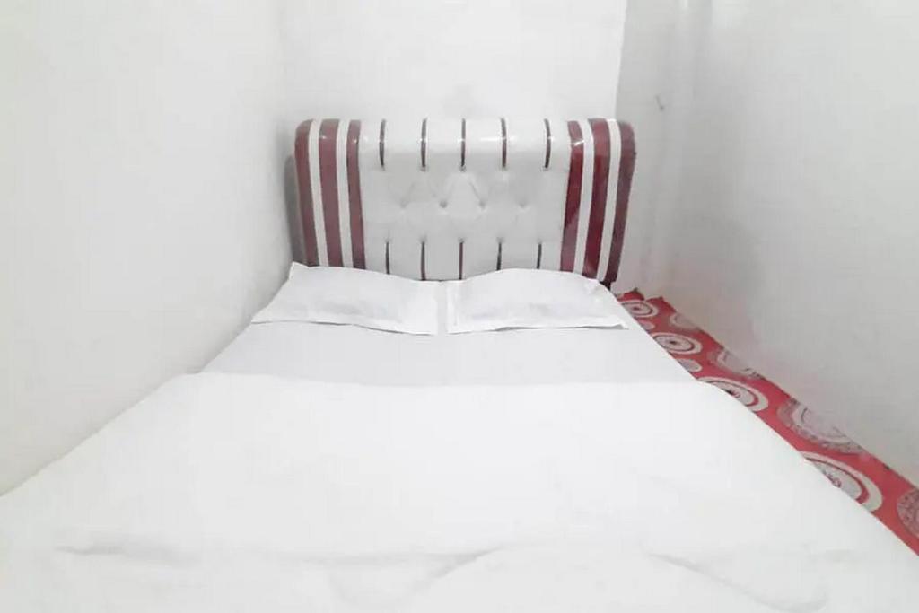 un letto bianco in una stanza con testiera a righe di Homestay Cantika Koto Tengah RedPartner a Sungaipenuh