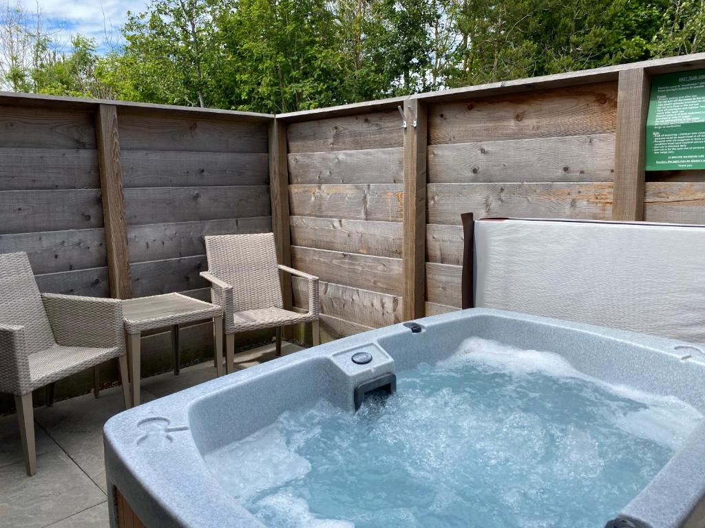 uma banheira de hidromassagem num pátio com cadeiras e uma cerca em Fox Lodge with Hot Tub em Cupar
