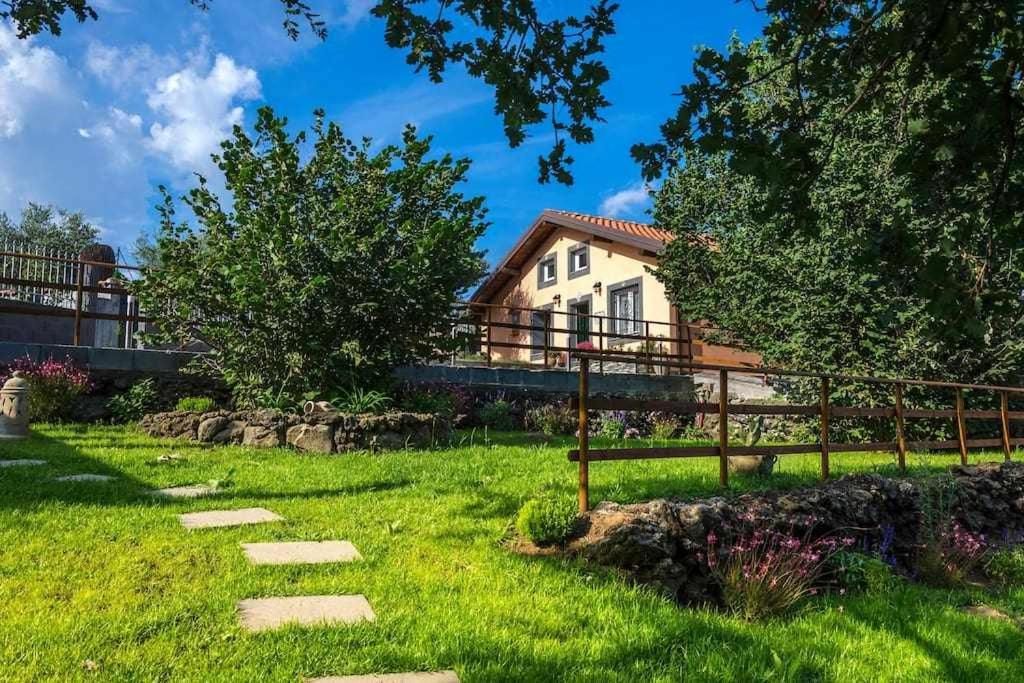 una casa sullo sfondo con un cortile verde di Villa del Gelso Chalet nel Parco dellEtna a Mascali