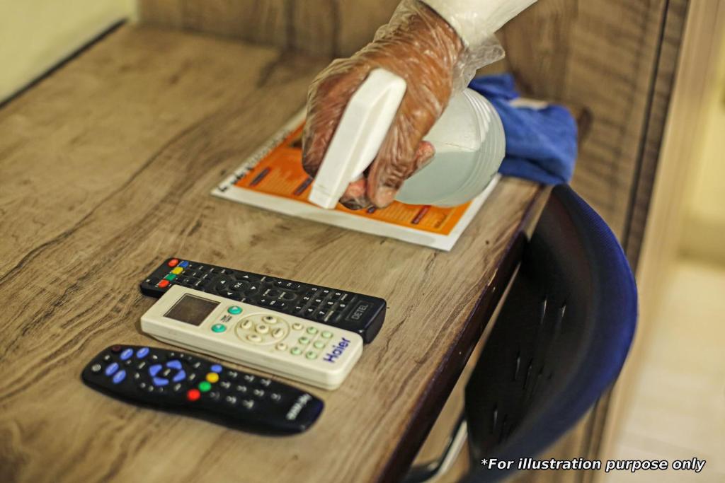two remote controls and a person holding a bottle on a table at OYO Flagship Hotel Daffodil Lodging and Boarding in Jānla