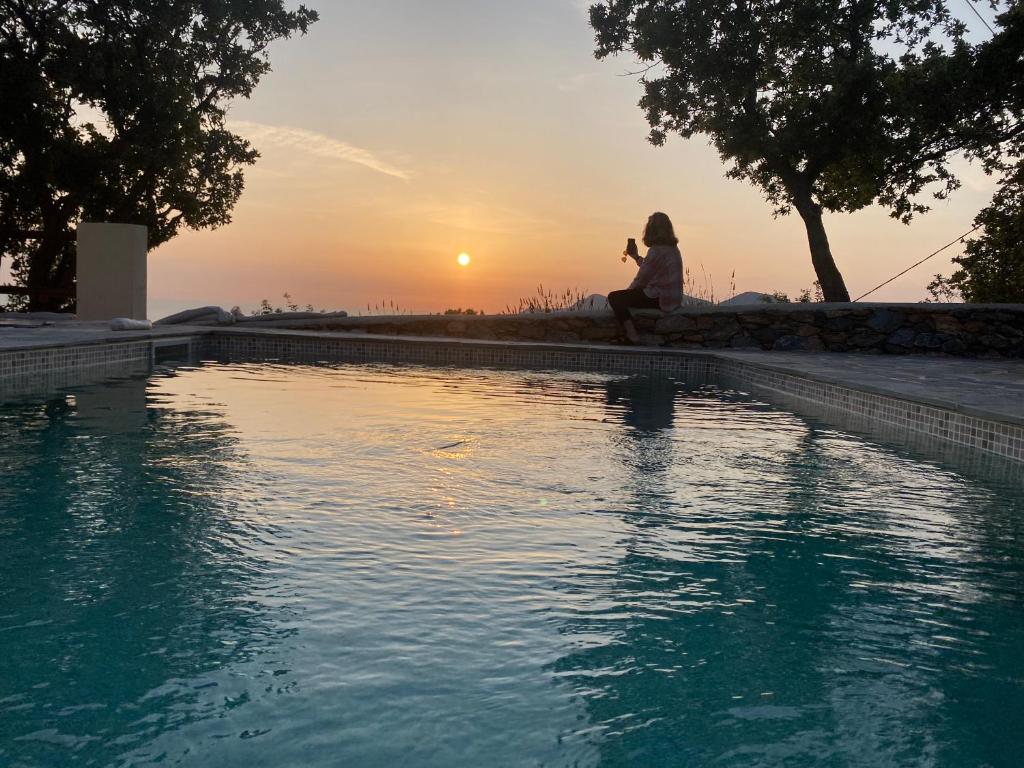 a woman sitting next to a swimming pool at sunset at VillaNova in Drymonas