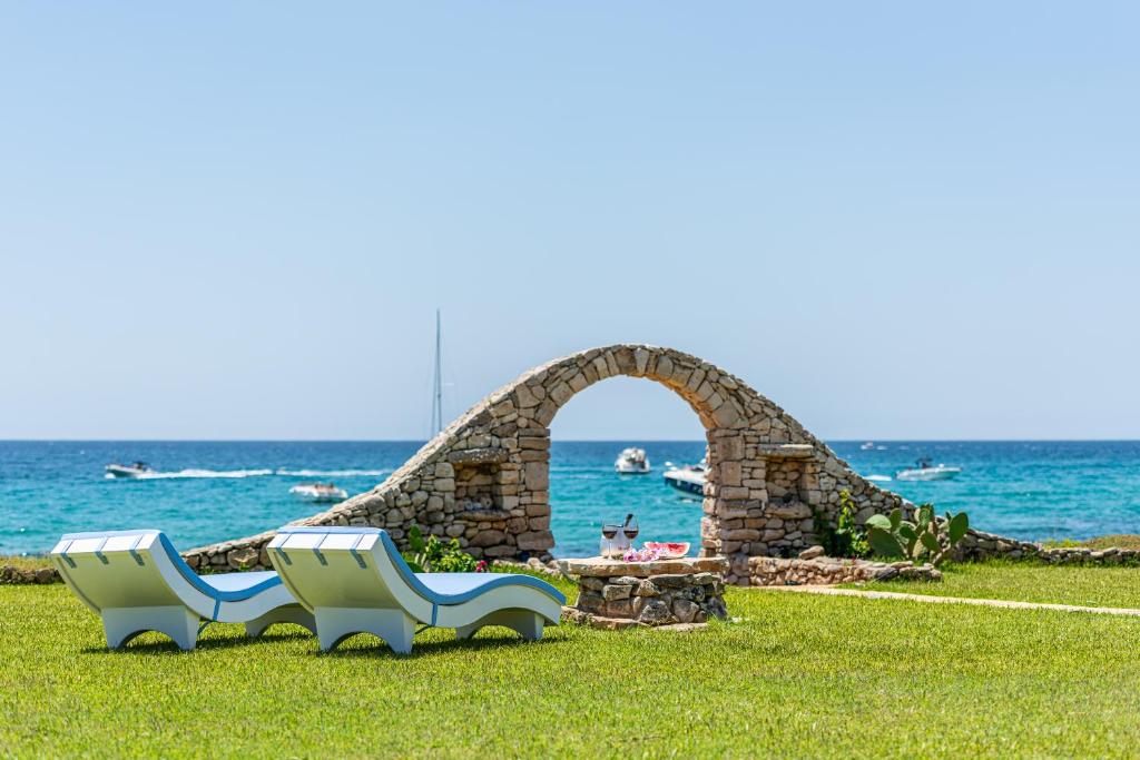 two white chairs sitting in the grass near the ocean at Villa Eva Luxury Leuca by EFFEsalento it in Leuca