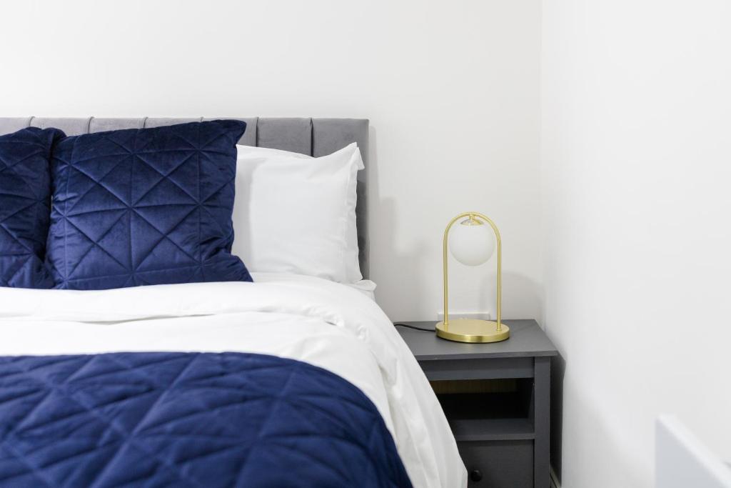 Chic Urban 2 Bedroom Apartments في كارديف: سرير لحاف ازرق وطاولة جانبية مع مصباح