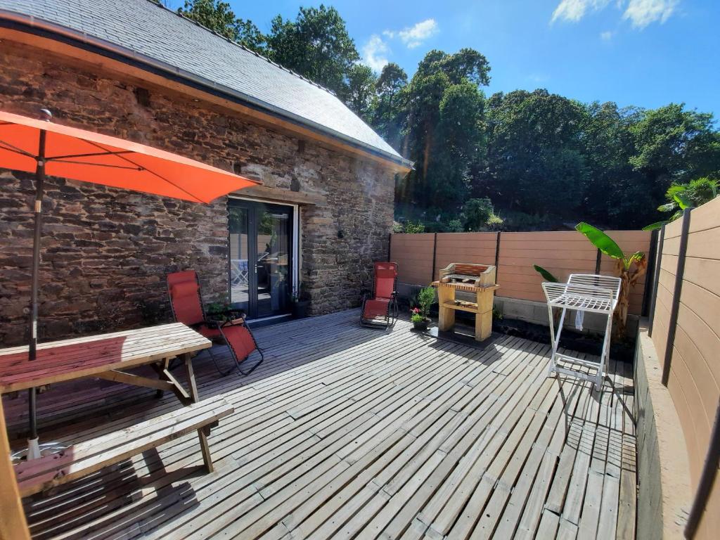 una terraza de madera con un banco y una sombrilla en A la Mémoire de Merlin & SPA en Saint-Malon-sur-Mel